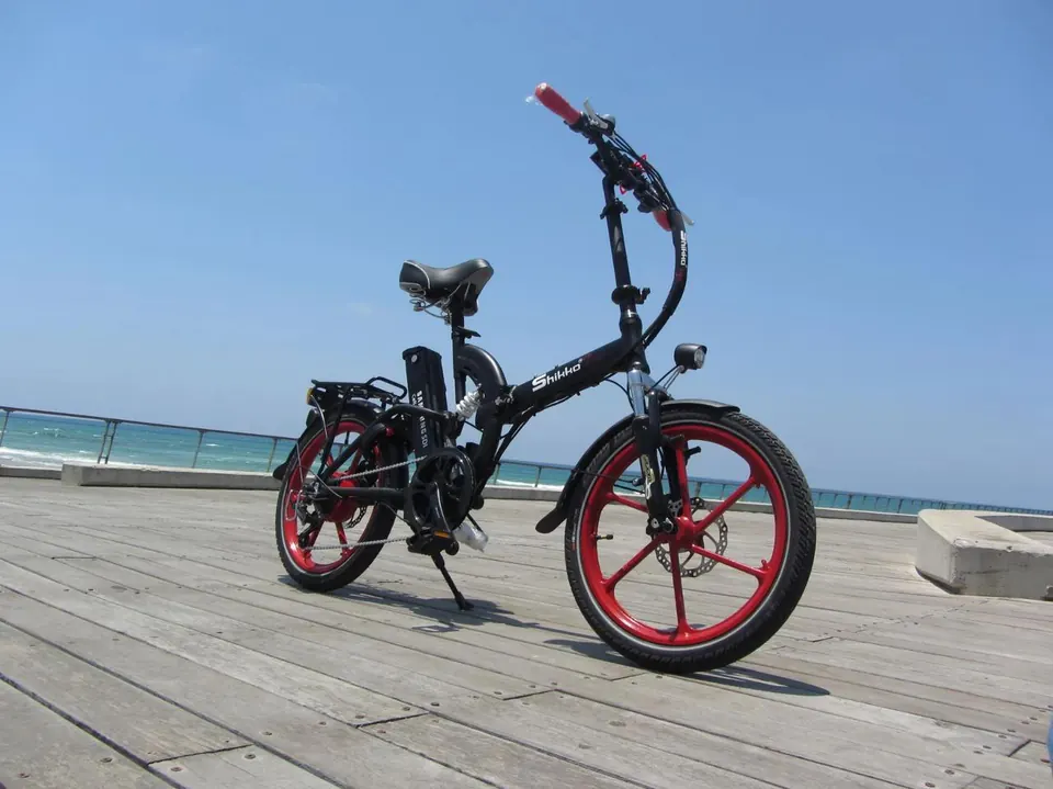 Black folding electric bike with red rims on a waterfront boardwalk